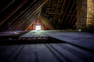 Old attic space with roof rafters and a window, shallow focus on wooden floor.