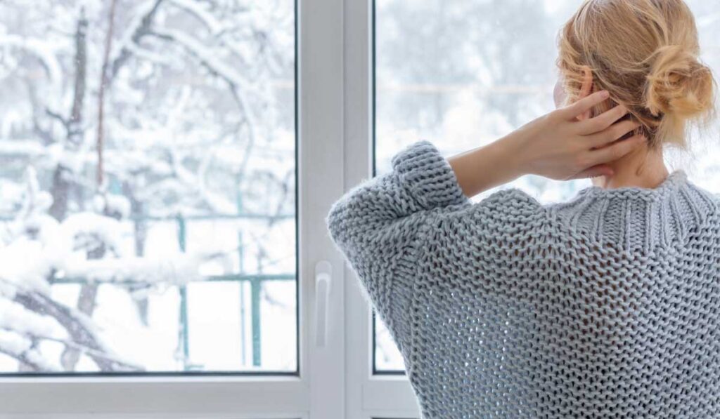 Woman standing in front of a snowy window, gazing outside.